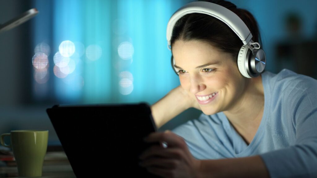 Woman in white headphones smiles while looking at glowing tablet | Embedding Network Effects