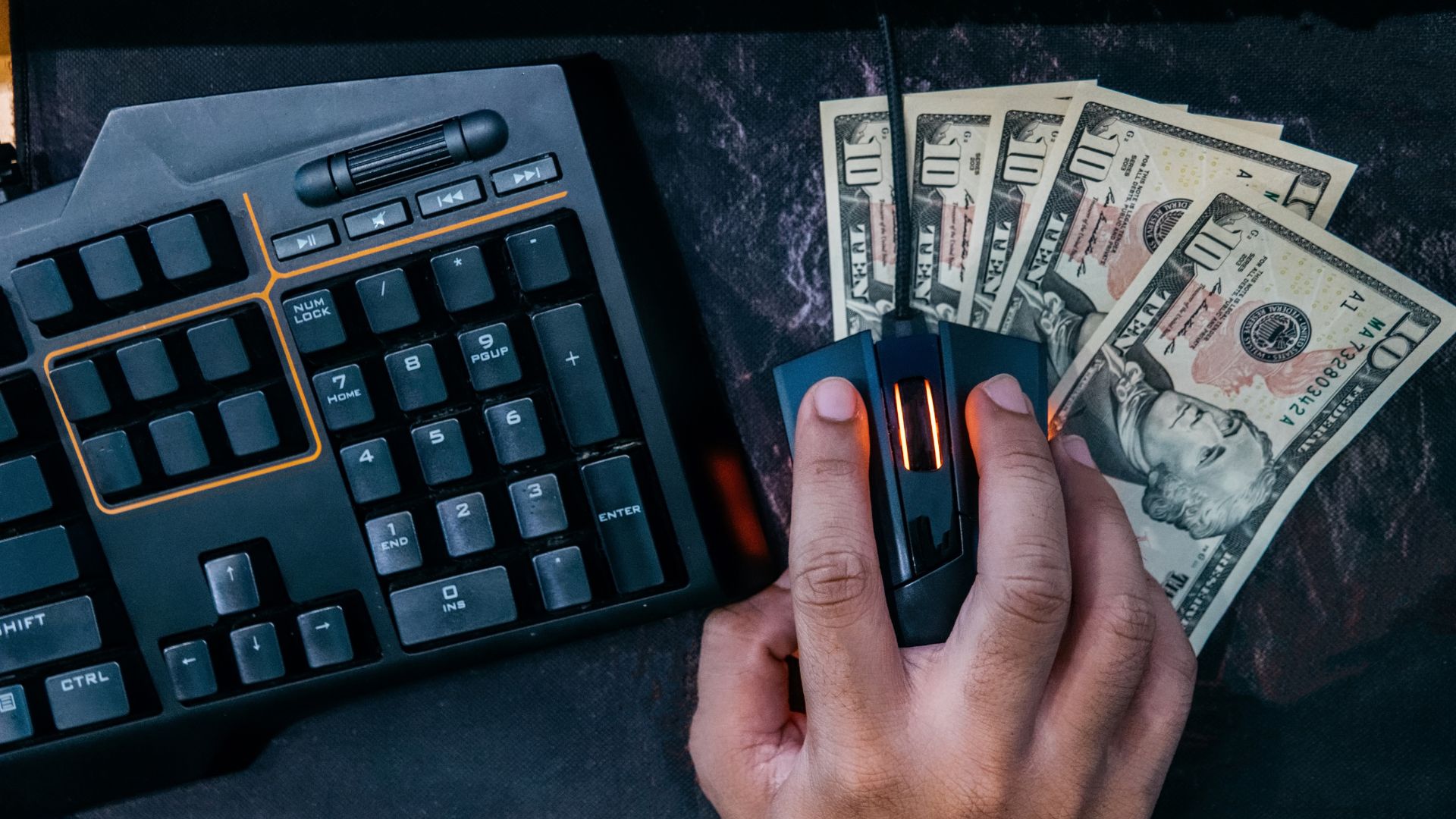 Close up of person holding computer mouse over ten-dollar bills and next to keyboard | Scale Effects for Product Defensibility