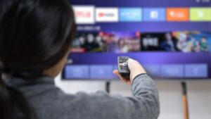 Woman holds remote up to TV with blurred movie titles | Embedding Network Effects