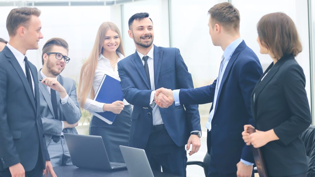 Two Men Shaking Hands During Group Meeting | Sales Growth Loops | Teknicks
