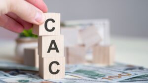 Close up of person stacking 3 tiny, wooden blocks that spell CAC | Customer Acquisition Costs