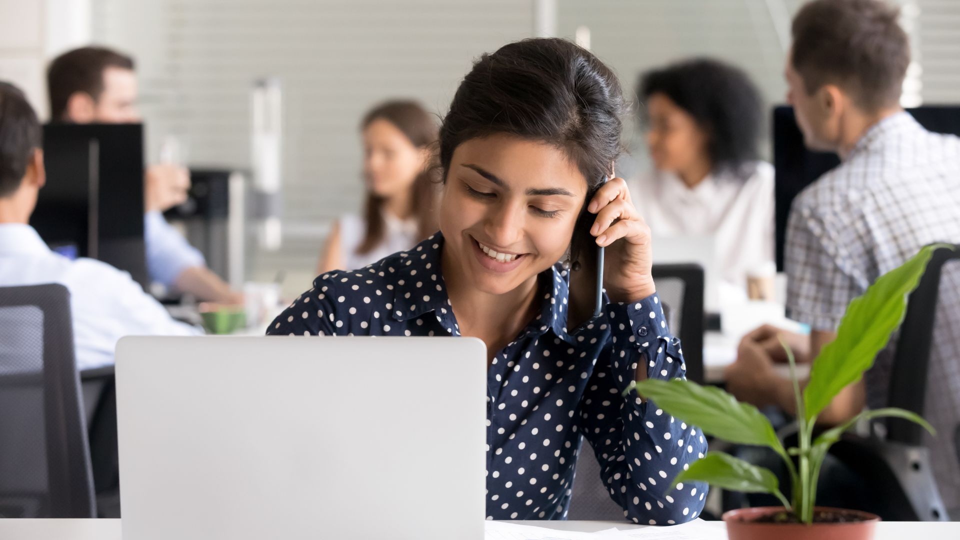 Woman smiles while talking on the phone and sitting in front of laptop | Leverage Brand Network Effects
