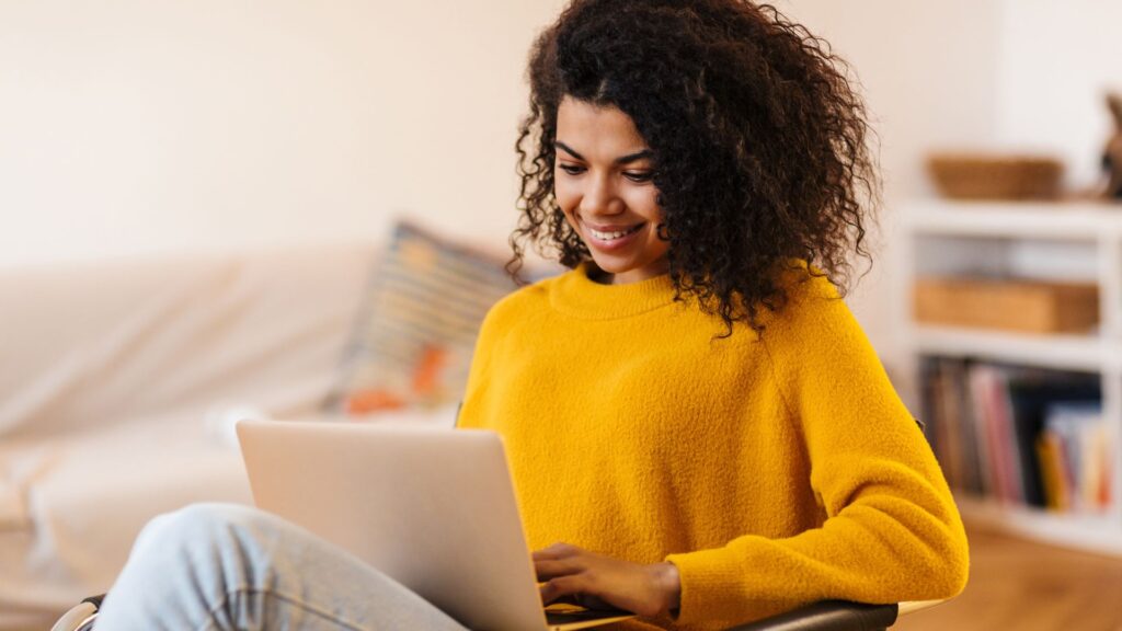 Woman in yellow sweater smiles while typing on laptop | User Activation for Streaming Companies