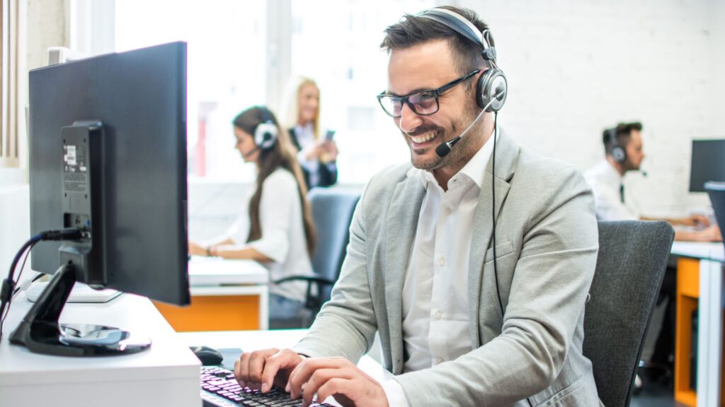 SaaS manager wearing headset smiles while typing on desktop computer | Scale Effects for Product Defensibility