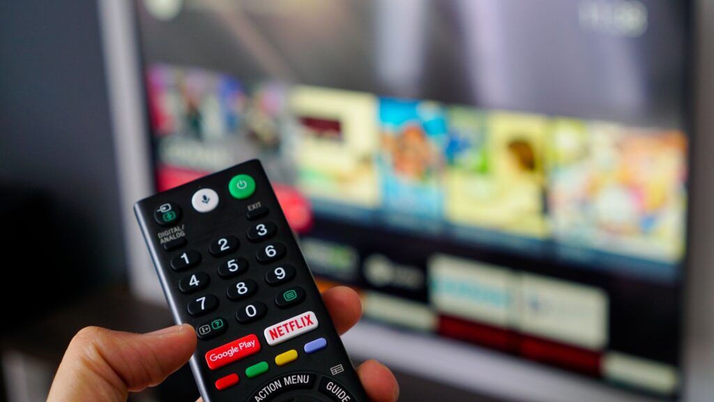 Close up of person holding remote over blurred TV in background | Embedding Network Effects