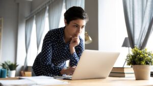 Woman holds chin while leaning over laptop as it rests on desk | User Resurrection for SaaS Companies