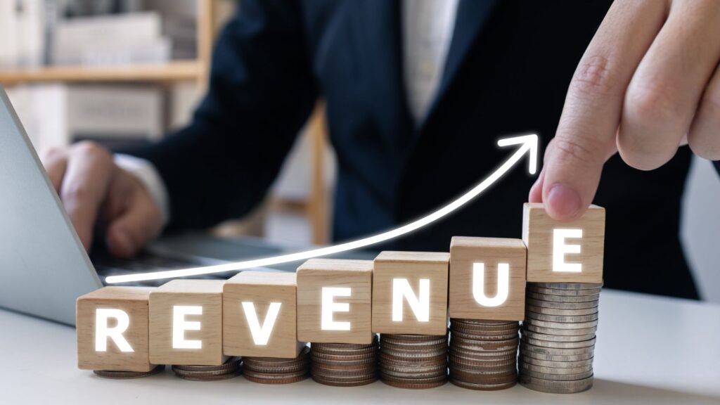 Wooden blocks spell 'Revenue' as they are placed on top of ascending coin stacks | ARPPU