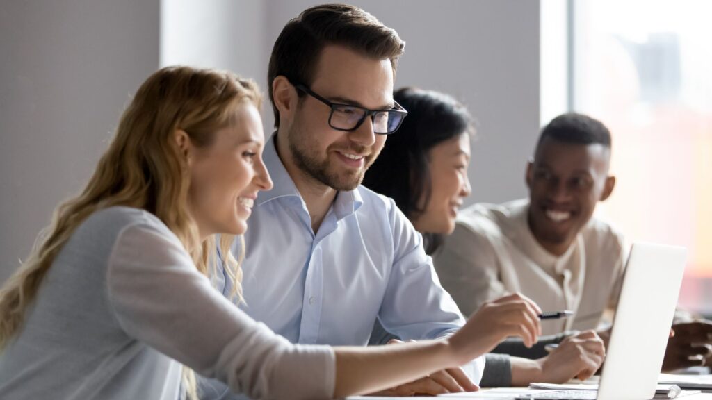 SaaS team smiles while collaboratively reviewing competitor strategy on laptop | Finding the Right SaaS Users