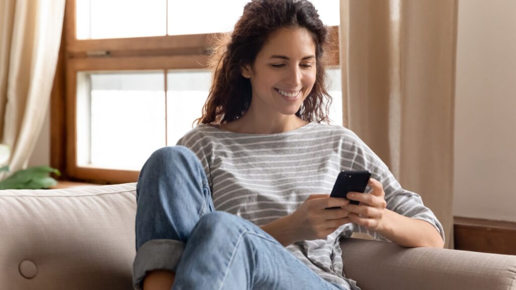 Woman smiles while sitting on couch and looking at smartphone | Finding the Right SaaS Users