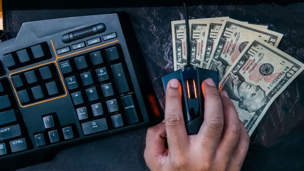 Close up of person holding computer mouse over ten-dollar bills and next to keyboard | Scale Effects for Product Defensibility