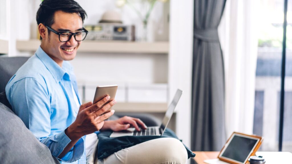 SaaS product user smiling while holding a smartphone and laptop | Scale Effects for Product Defensibility