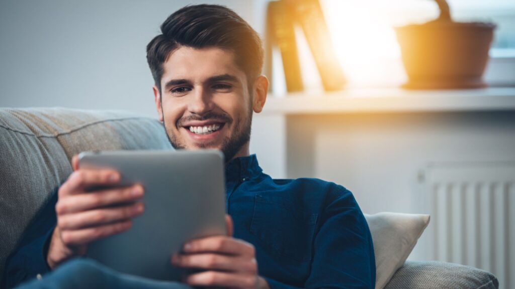 Man in blue shirt smiles while looking at silver tablet | User Activation for Streaming Companies